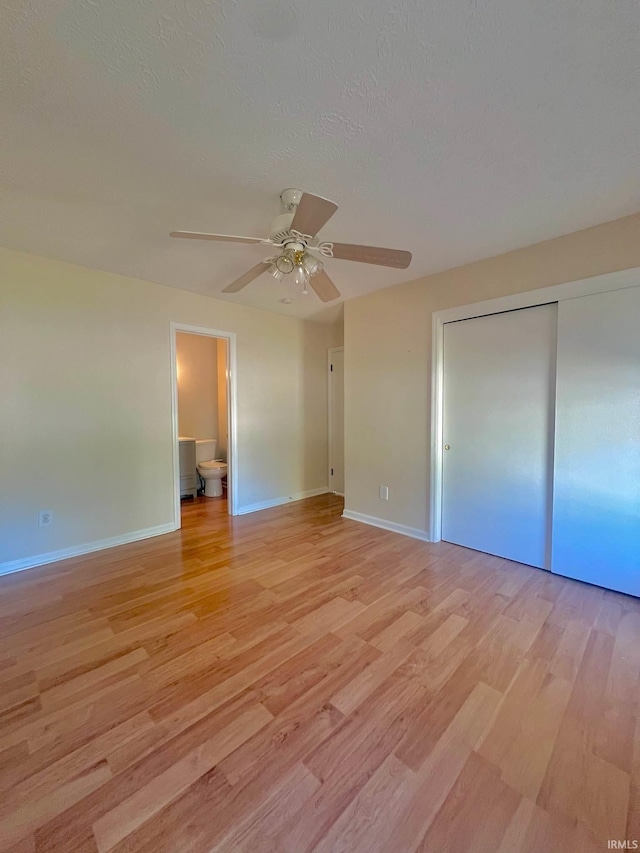 unfurnished bedroom with a closet, ceiling fan, ensuite bathroom, and light wood-type flooring