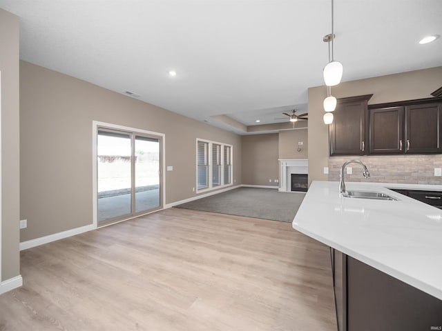 kitchen with dark brown cabinetry, pendant lighting, ceiling fan, sink, and light hardwood / wood-style flooring