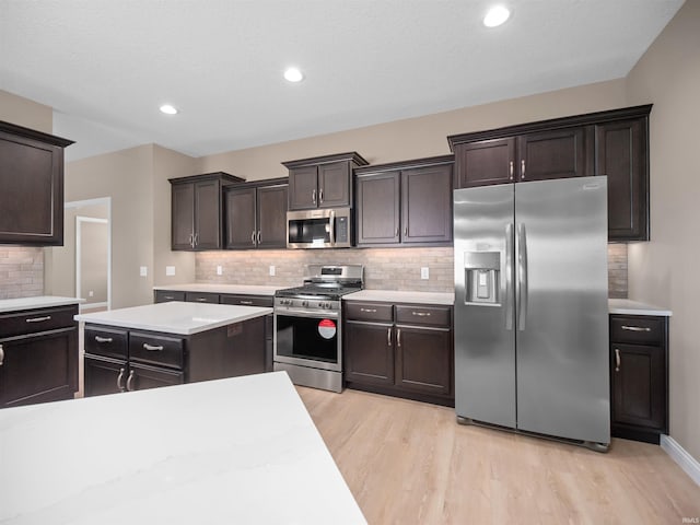 kitchen featuring appliances with stainless steel finishes, light wood-type flooring, dark brown cabinetry, and tasteful backsplash