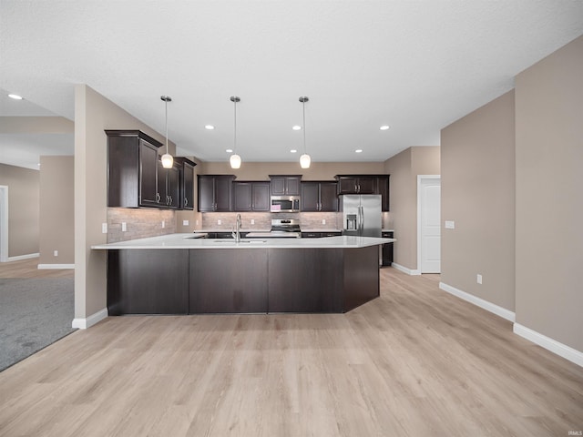 kitchen with dark brown cabinetry, light wood-type flooring, appliances with stainless steel finishes, and hanging light fixtures