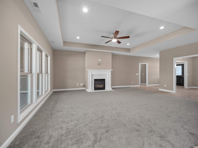 unfurnished living room with light colored carpet, ceiling fan, and a raised ceiling