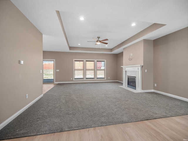 unfurnished living room with ceiling fan, a wealth of natural light, light hardwood / wood-style floors, and a raised ceiling