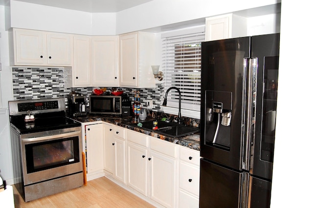 kitchen featuring white cabinets, appliances with stainless steel finishes, dark stone countertops, light wood-type flooring, and decorative backsplash