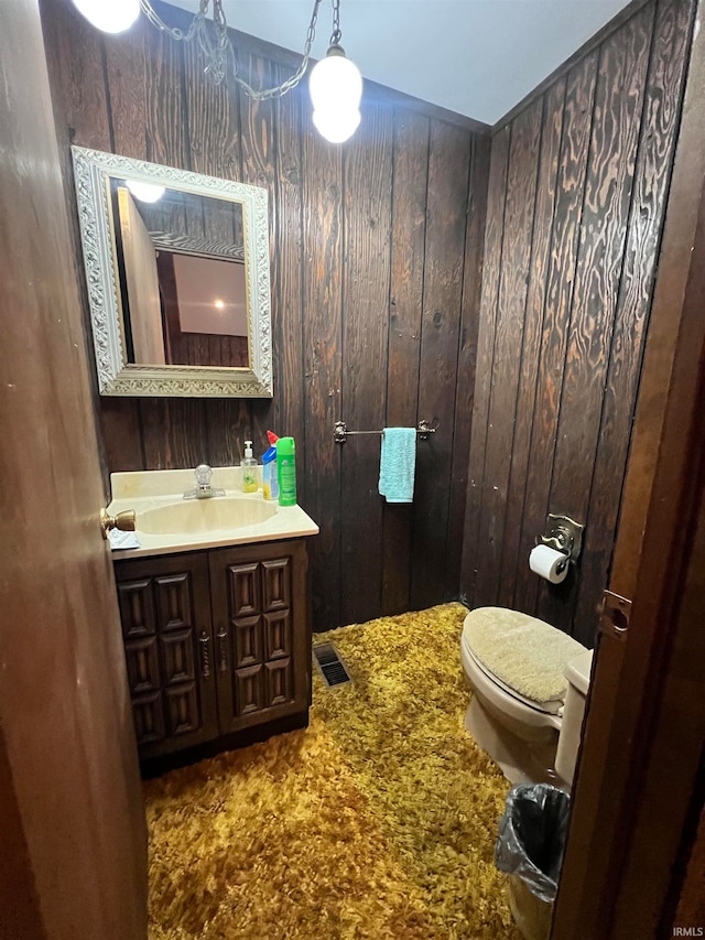 bathroom with lofted ceiling, vanity, wood walls, and toilet