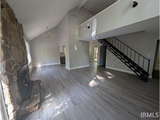 unfurnished living room with a notable chandelier, high vaulted ceiling, a stone fireplace, and dark hardwood / wood-style flooring