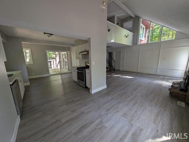 kitchen with wood-type flooring, white cabinets, stainless steel range with electric stovetop, and high vaulted ceiling