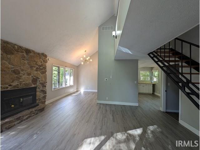 unfurnished living room featuring high vaulted ceiling, a stone fireplace, wood-type flooring, an inviting chandelier, and a textured ceiling