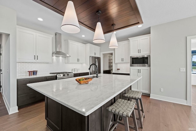 kitchen featuring an island with sink, wall chimney range hood, and white cabinetry