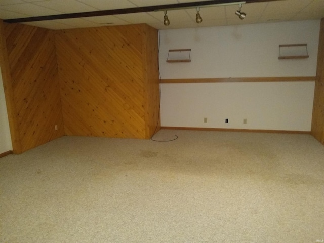 basement with a drop ceiling, carpet, and wooden walls