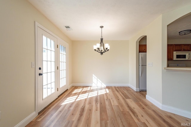 unfurnished dining area with light hardwood / wood-style floors, a notable chandelier, and a textured ceiling