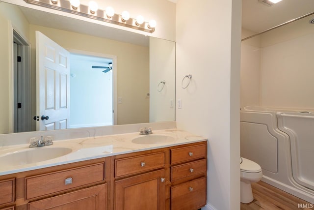 full bathroom with ceiling fan, vanity, hardwood / wood-style flooring,  shower combination, and toilet