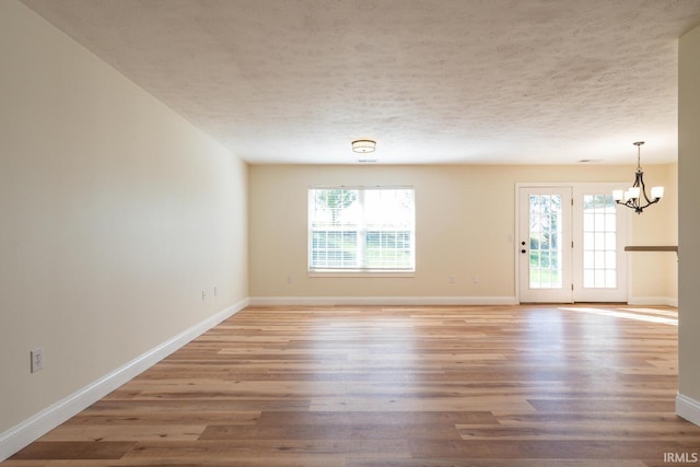 empty room with an inviting chandelier, light hardwood / wood-style floors, and a textured ceiling