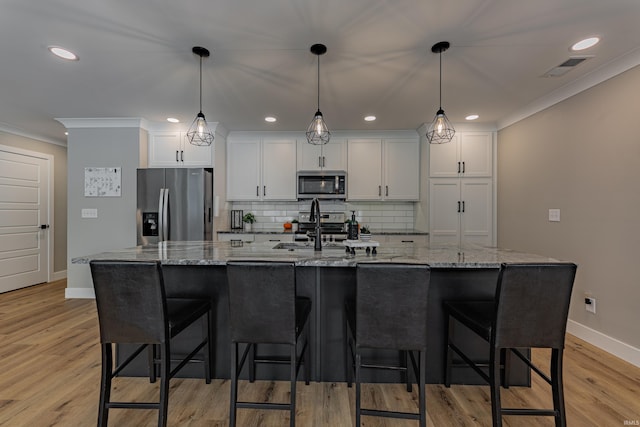 kitchen with white cabinetry, appliances with stainless steel finishes, decorative light fixtures, and a large island with sink