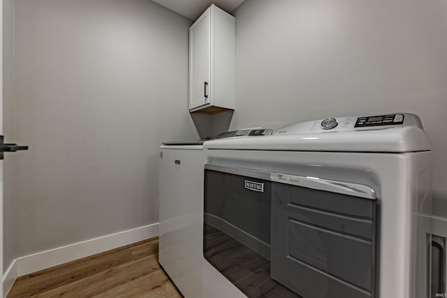 laundry area featuring independent washer and dryer, light hardwood / wood-style flooring, and cabinets