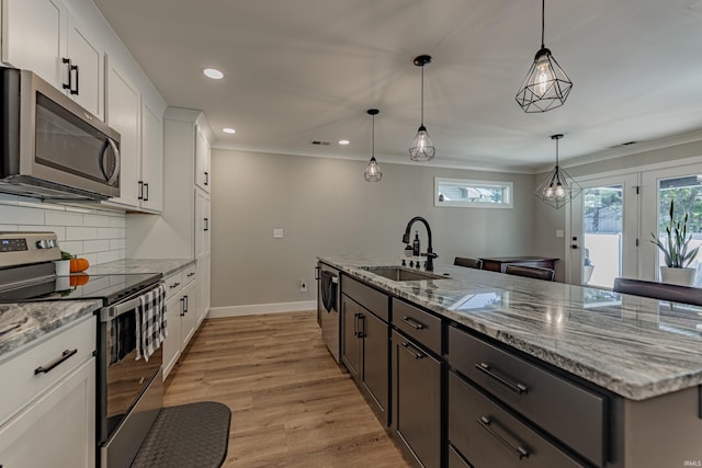 kitchen with pendant lighting, sink, appliances with stainless steel finishes, white cabinetry, and an island with sink