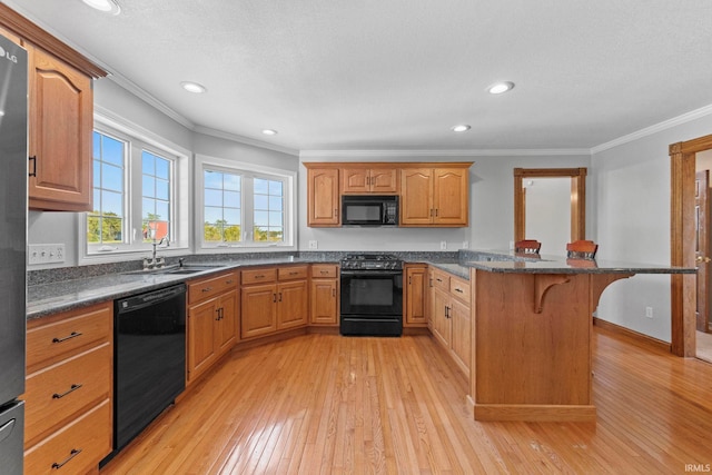 kitchen featuring black appliances, sink, light hardwood / wood-style floors, crown molding, and a breakfast bar area