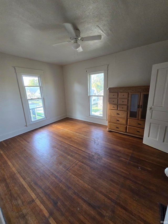 unfurnished room with ceiling fan, a textured ceiling, plenty of natural light, and dark hardwood / wood-style floors