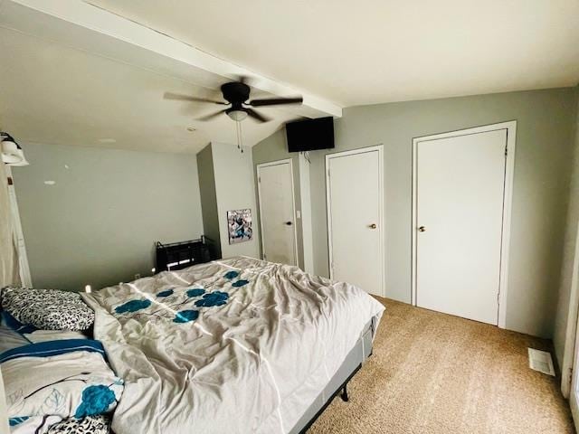 carpeted bedroom featuring multiple closets, vaulted ceiling with beams, and ceiling fan