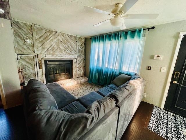 living room featuring a large fireplace, dark wood-type flooring, a textured ceiling, and ceiling fan