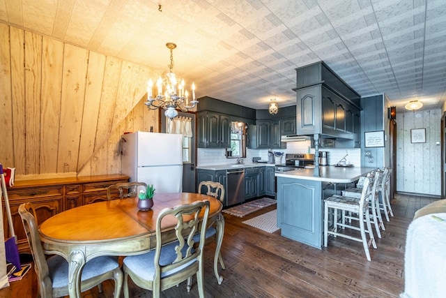 kitchen with dark hardwood / wood-style flooring, decorative light fixtures, sink, wooden walls, and stainless steel appliances