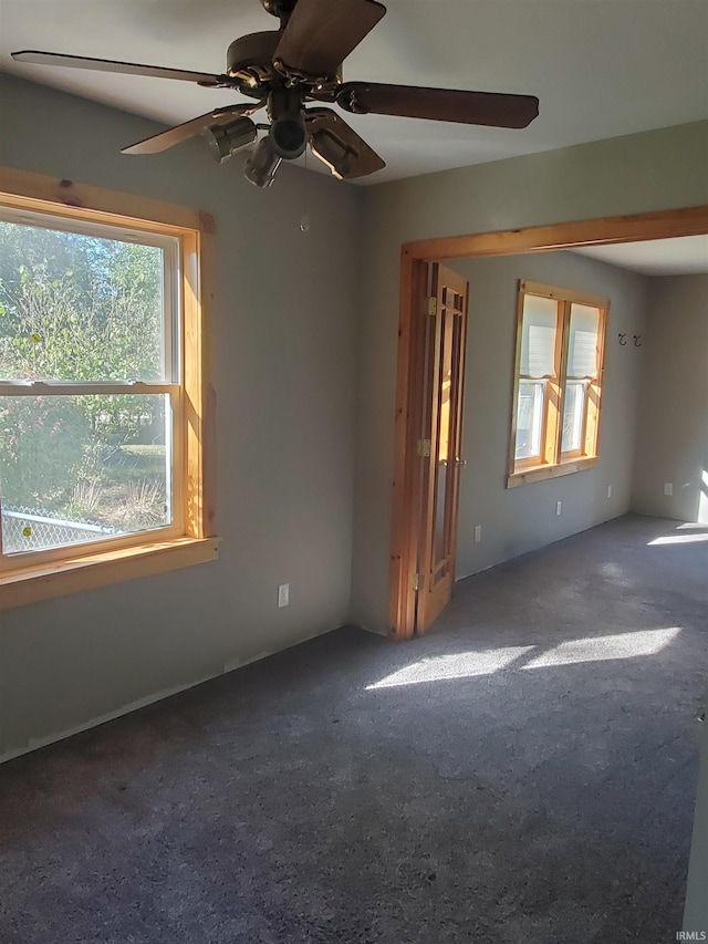 spare room featuring ceiling fan, dark carpet, and a wealth of natural light