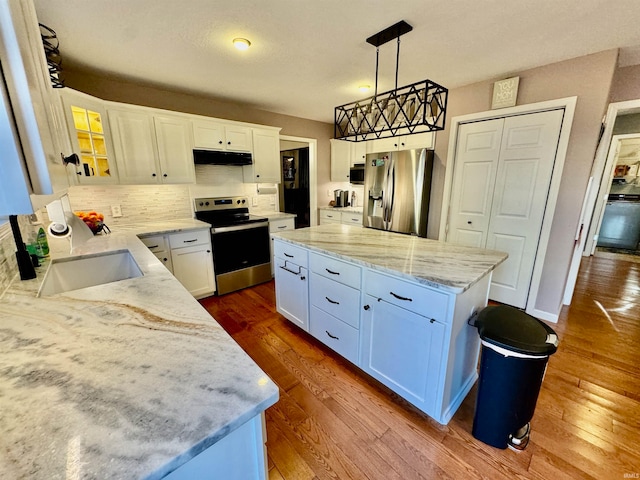 kitchen featuring stainless steel appliances, sink, decorative light fixtures, white cabinets, and a center island