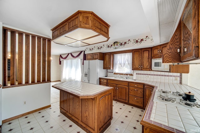 kitchen featuring a center island, white appliances, sink, tile counters, and backsplash