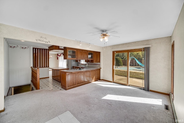 kitchen with kitchen peninsula, light colored carpet, rail lighting, and ceiling fan