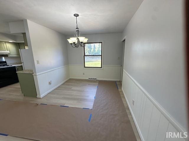 unfurnished dining area with a notable chandelier and light wood-type flooring