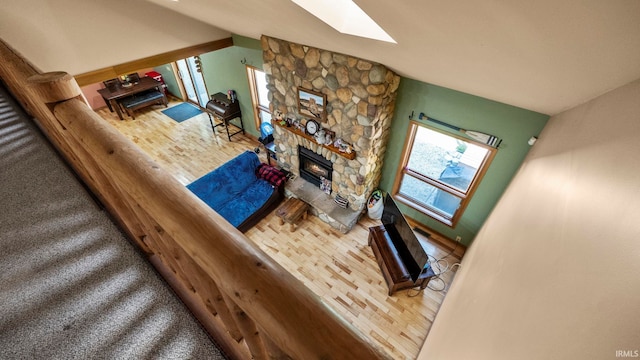 living room with vaulted ceiling with skylight, wood-type flooring, and a stone fireplace