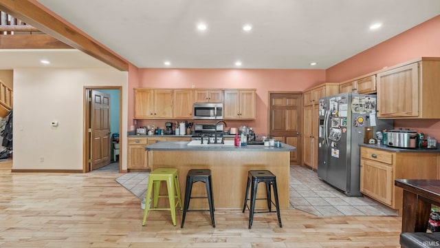 kitchen with light brown cabinetry, light hardwood / wood-style flooring, a center island with sink, stainless steel appliances, and a kitchen bar