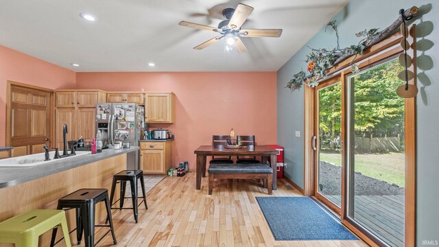 kitchen featuring stainless steel fridge, light wood-type flooring, ceiling fan, light brown cabinetry, and a kitchen breakfast bar