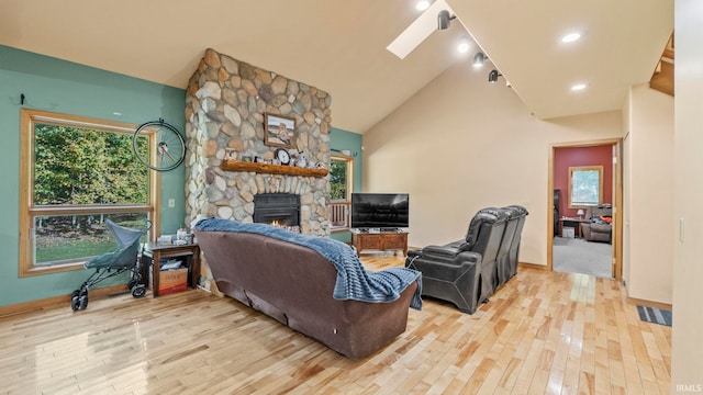 living room with a skylight, light wood-type flooring, a fireplace, and high vaulted ceiling