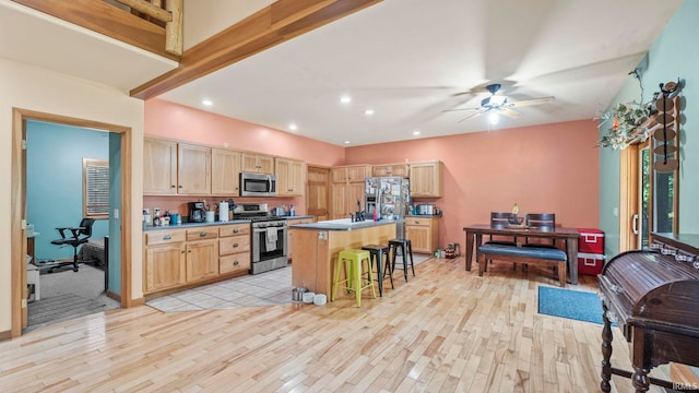 kitchen with light wood-type flooring, a center island, stainless steel appliances, light brown cabinetry, and a kitchen breakfast bar