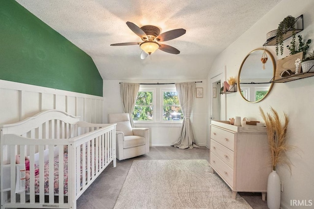 carpeted bedroom featuring lofted ceiling, a nursery area, a textured ceiling, and ceiling fan