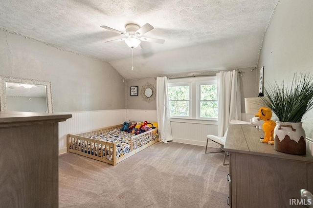 carpeted bedroom with a nursery area, ceiling fan, vaulted ceiling, and a textured ceiling