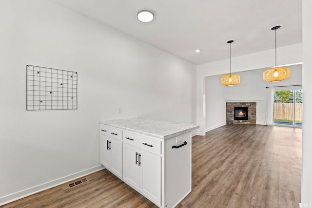 kitchen with pendant lighting, white cabinets, light wood-type flooring, and a stone fireplace