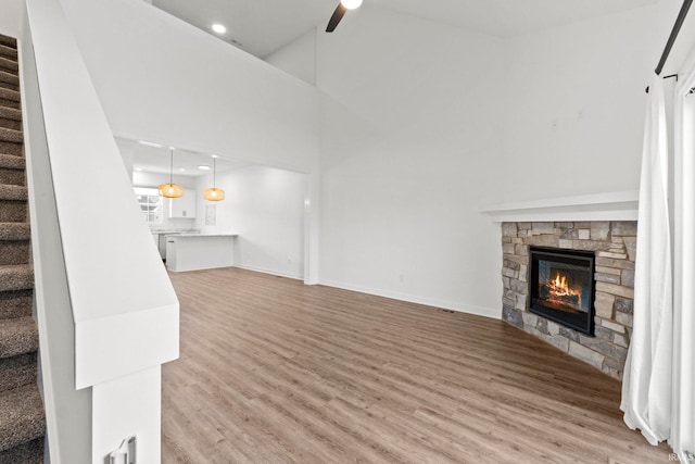 unfurnished living room featuring a towering ceiling, plenty of natural light, light wood-type flooring, and a stone fireplace