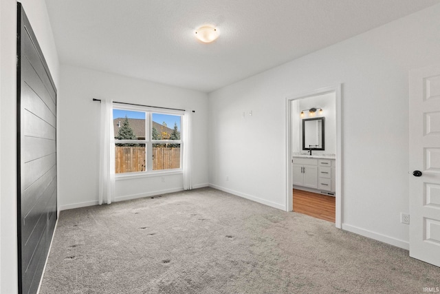 unfurnished bedroom with ensuite bathroom, sink, and light colored carpet