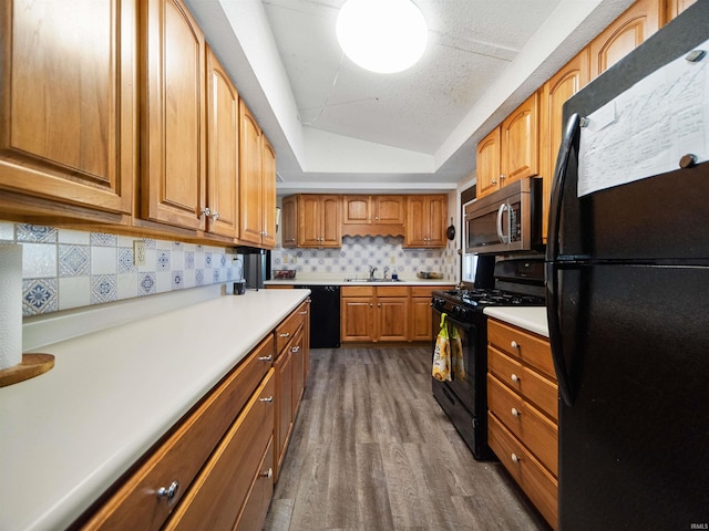 kitchen with tasteful backsplash, dark hardwood / wood-style flooring, a raised ceiling, sink, and black appliances