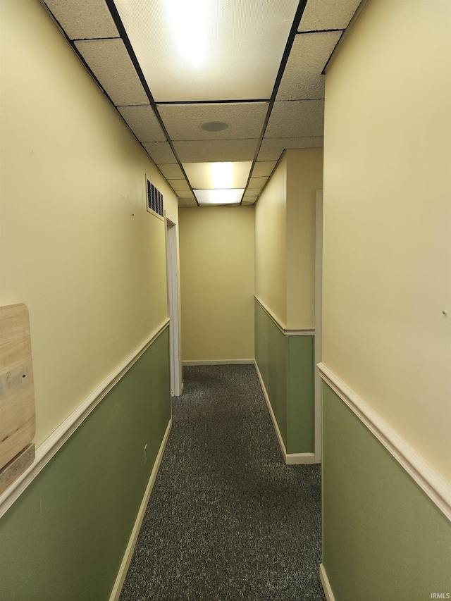 corridor featuring a paneled ceiling and dark carpet