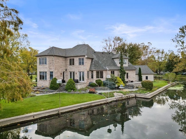 rear view of house featuring a water view and a lawn