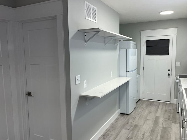 laundry room with light hardwood / wood-style flooring and stacked washer / drying machine