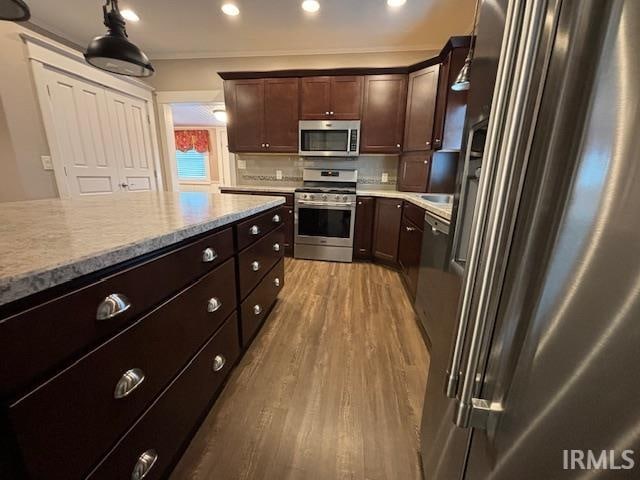 kitchen with dark brown cabinetry, hardwood / wood-style floors, tasteful backsplash, appliances with stainless steel finishes, and decorative light fixtures