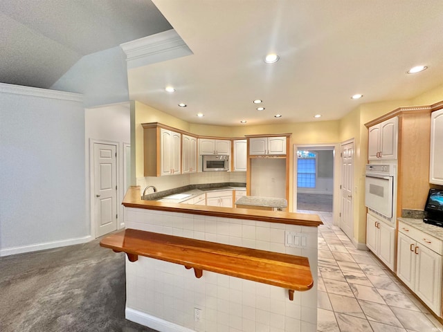 kitchen with kitchen peninsula, ornamental molding, light brown cabinetry, white oven, and light colored carpet