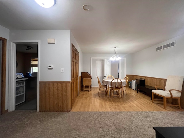 dining area with light carpet, a notable chandelier, and wooden walls