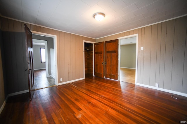 unfurnished bedroom with ornamental molding, wood walls, and dark hardwood / wood-style flooring