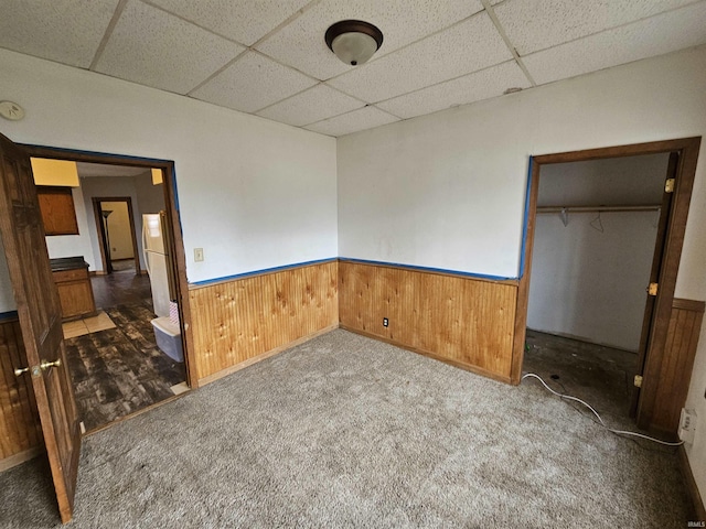 unfurnished bedroom with wooden walls, carpet flooring, a drop ceiling, white fridge, and a closet