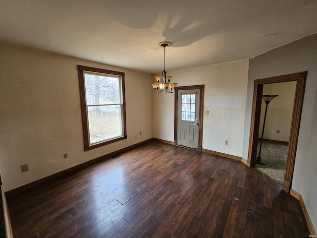 empty room featuring a notable chandelier, dark wood-type flooring, and a wealth of natural light