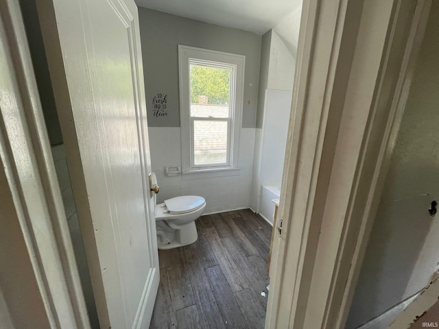 bathroom featuring tile walls, hardwood / wood-style floors, a bathing tub, and toilet